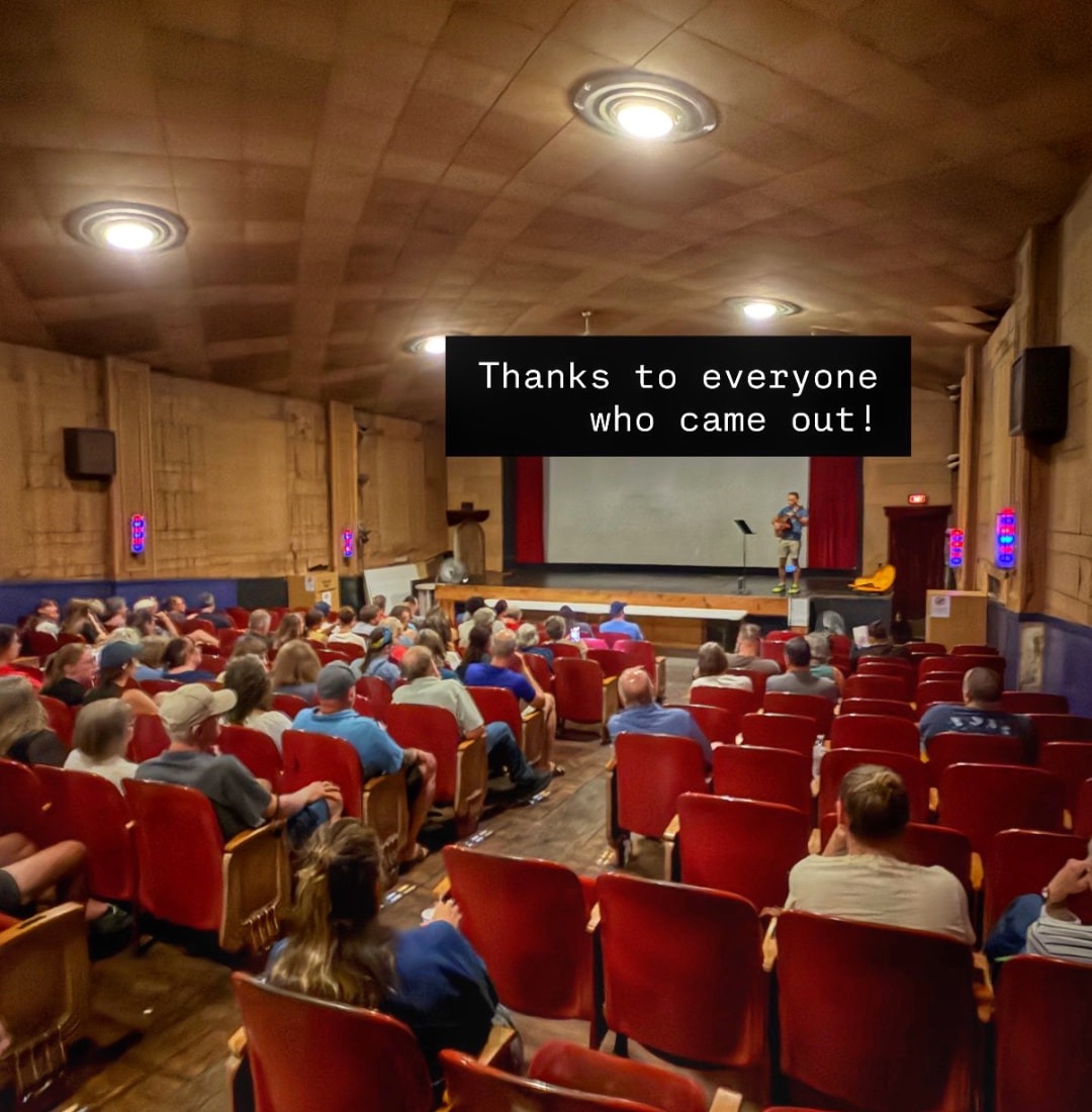 Inside a local theater after the Float Nebraska screening: a performer with an acoustic guitar on stage, a full house of red seats, and the words “Thanks to everyone who came out!”